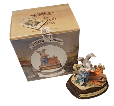 Leonardo Bunny figurine - The Creative Shed - The Creative Shed - A Leonardo Bunny figurine next to its packaging box, featuring the figurine on a base with a floral pattern, holding a carrot, with the box showing a picture of the figurine and the brand 'Rabbit Village'. - 