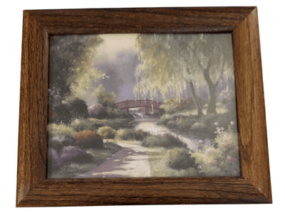 Red Bridge print - The Creative Shed - The Creative Shed - A framed artwork depicting a red bridge in a green, lush outdoor setting with trees and a pathway. - 